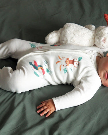 Bébé qui dort sur son lit avec le pyjama de la collection jungle.