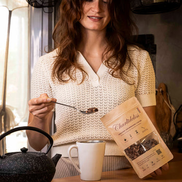 Femme rousse se servant une cuillère de l'infusion charlidéliss pour la mettre dans sa tasse et rajouter l'eau bouillante de sa théière. C'est la meilleure tisane anti-stress à base de cosses de cacao issue de la production de notre complément alimentaire chocolatée. 
