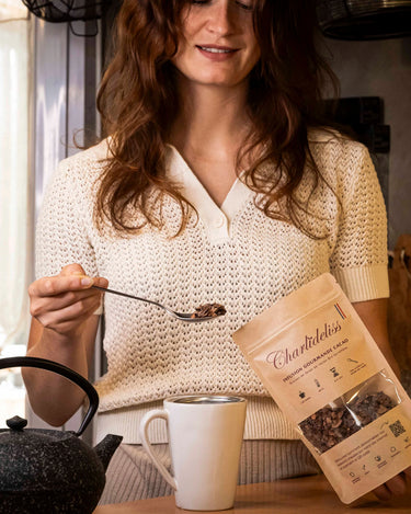 Femme rousse se servant une cuillère de l'infusion charlidéliss pour la mettre dans sa tasse et rajouter l'eau bouillante de sa théière. C'est la meilleure tisane anti-stress à base de cosses de cacao issue de la production de notre complément alimentaire chocolatée. 