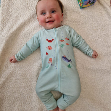Bébé allongé sur tapis et souriant portant le pyjama "nager au lieu des coraux" de la collection mer.