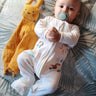 Bébé portant le pyjama "pétillant comme un toucan" de la collection Jungle avec présence de son doudou à côté.