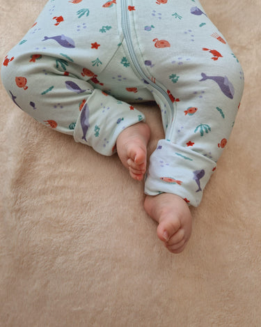 Focus sur la partie bas du corps du bébé présentant les pieds à l'air avec les chaussettes retroussables ouvertes.